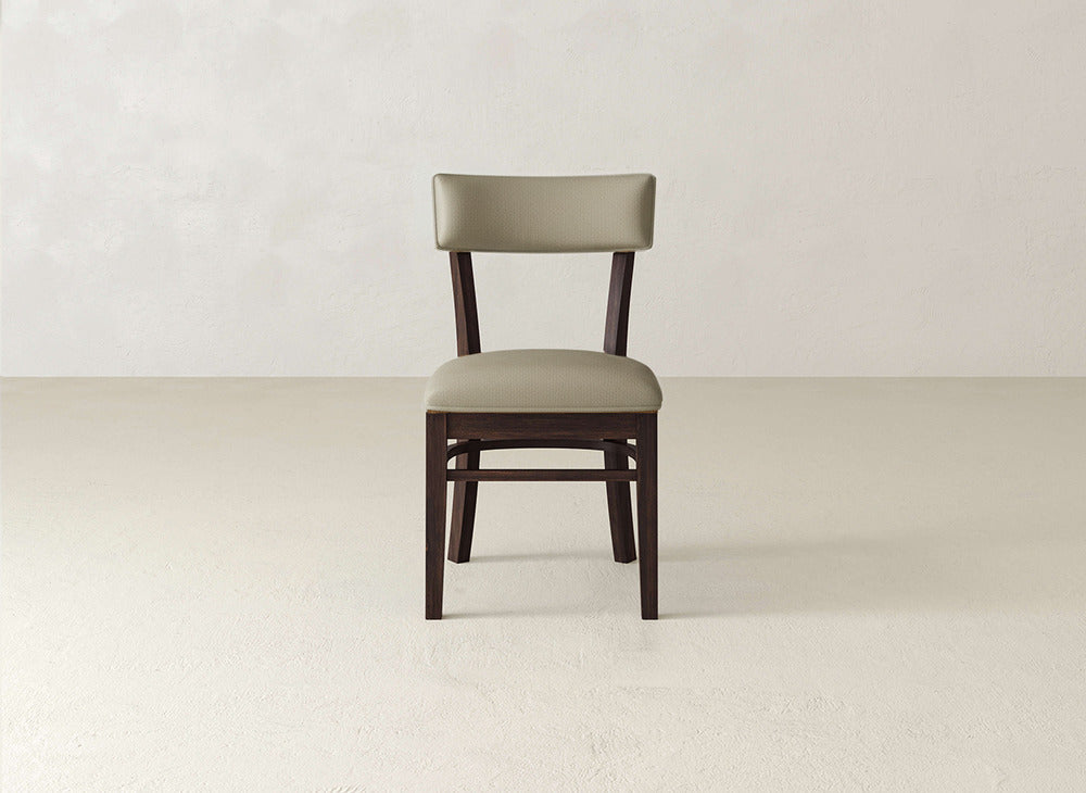 The Everly Side Dining Chair by James+James features a padded light brown seat and backrest, shown on a light floor against a neutral, textured wall.
