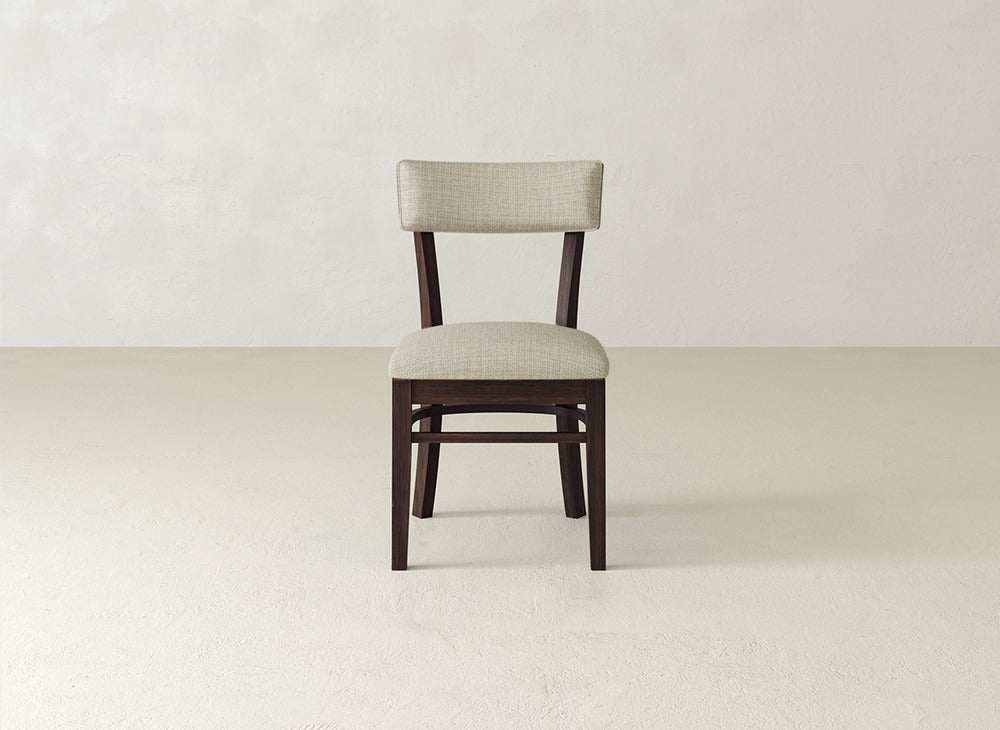 The Everly Side Dining Chair by James+James features a cushioned beige seat and backrest, showcased in the center of a simple, light-toned room with a minimal background.