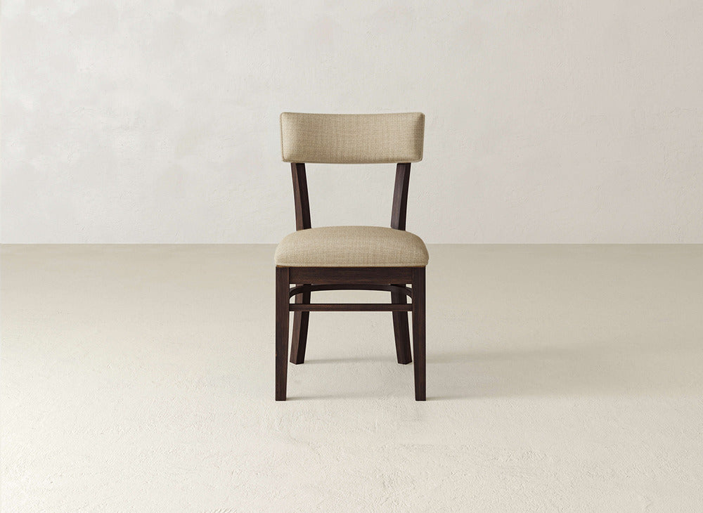 The Everly Side Dining Chair by James+James features a simple wooden frame with a beige upholstered seat and backrest, shown on a light floor against a plain background.