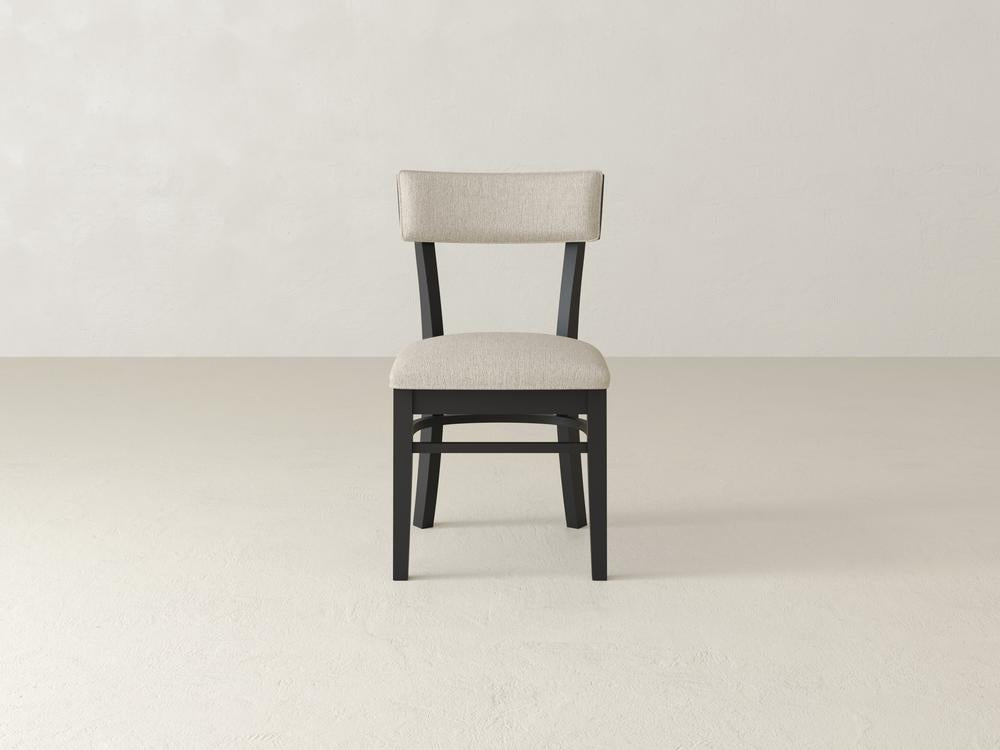A single chair with a beige cushioned seat and backrest, supported by a dark wooden frame, is centered against a plain, light-colored background. The setting is minimalistic and modern.