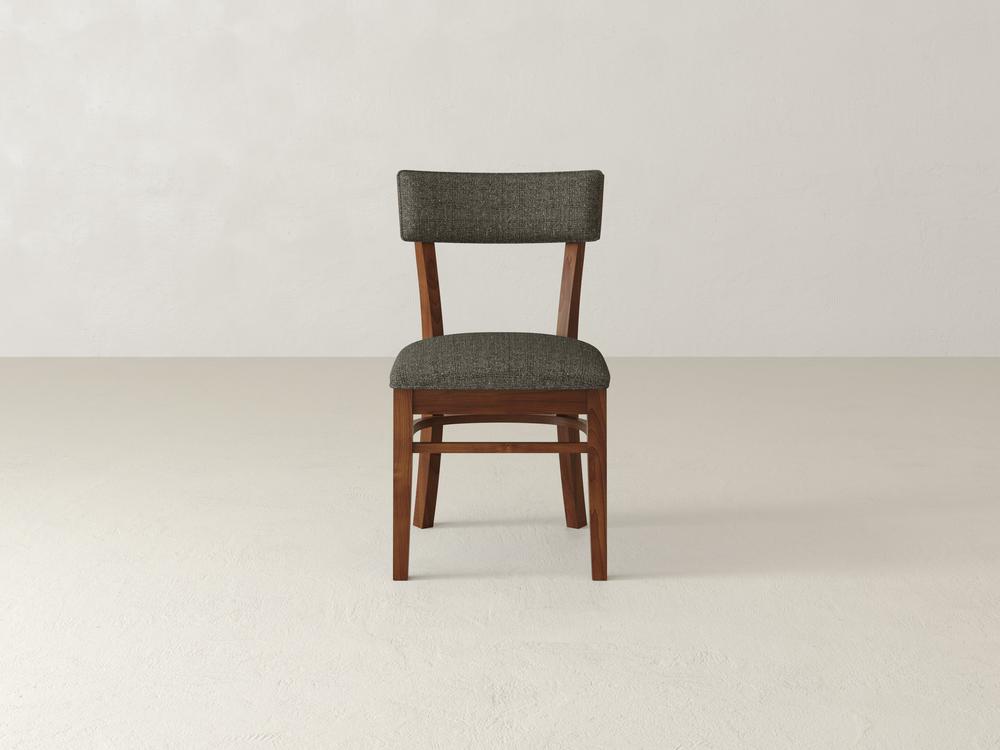 A wooden chair with a cushioned seat and backrest upholstered in dark gray fabric, placed on a light-colored floor against a plain white wall. The design is simple and classic.