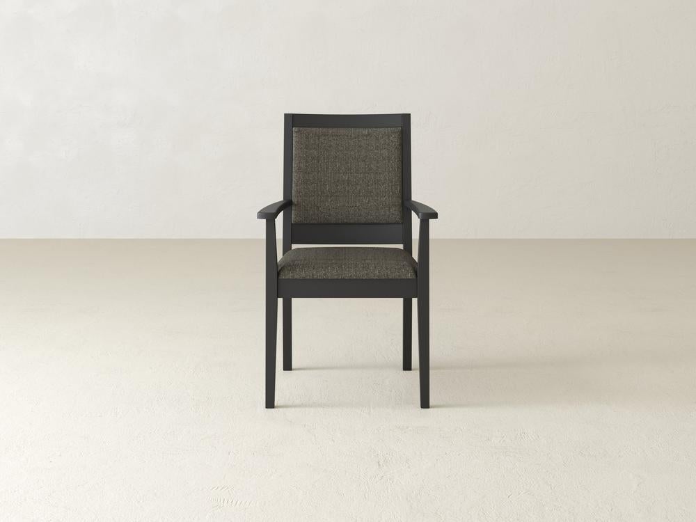 A single wooden chair with dark frame and textured gray cushion is centered in the image. The background is a plain, light-colored wall and floor.
