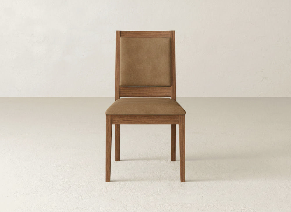 The Gina Side Dining Chair by James+James, featuring a maple wood frame and light brown cushioned seat and backrest, is placed on a plain, light-colored floor against an off-white wall.