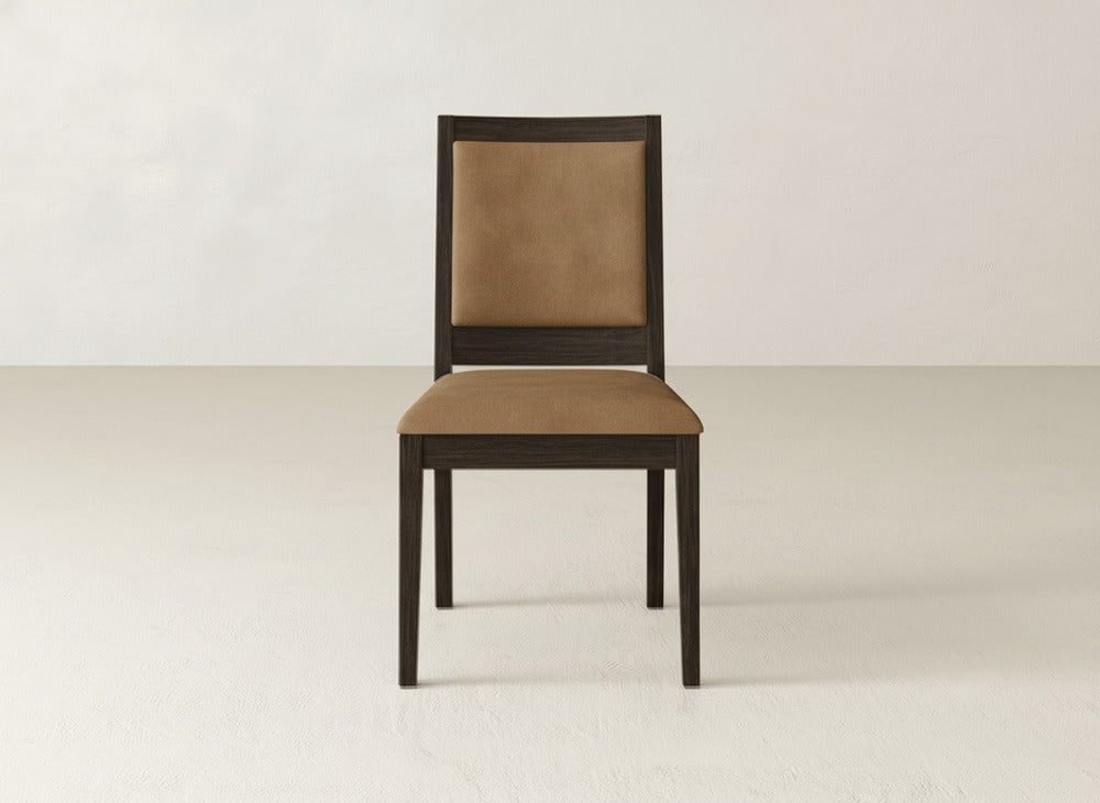The James+James Gina Side Dining Chair, made from maple with a brown cushioned seat and backrest, is shown in an empty light-colored room against a plain wall.