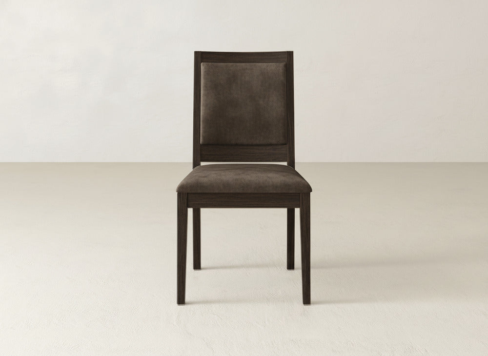 A single Gina Side Dining Chair by James+James, made of rich maple and featuring matching brown padded upholstery on the seat and backrest, sits centered in a minimalist room with light walls and flooring.