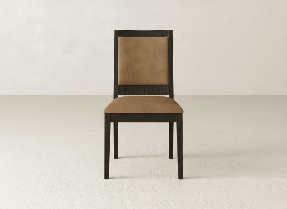 A James+James Gina Side Dining Chair featuring a dark maple wood frame and light brown cushioned seat and backrest is set against a plain, light-colored wall and floor.