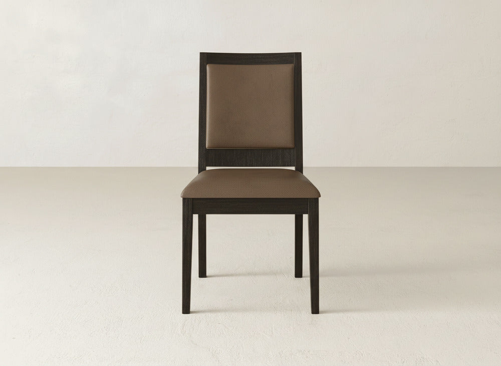 A James+James Gina Side Dining Chair with a dark maple frame and brown cushioned seat and backrest sits on a light floor against an off-white wall.
