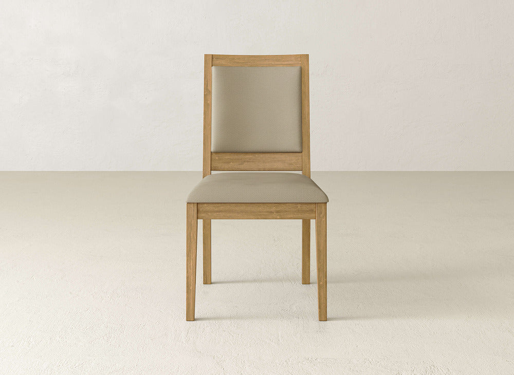 The James+James Gina Side Dining Chair, crafted from maple wood with a light brown cushioned seat and backrest, is shown on a plain, light floor against an off-white wall.