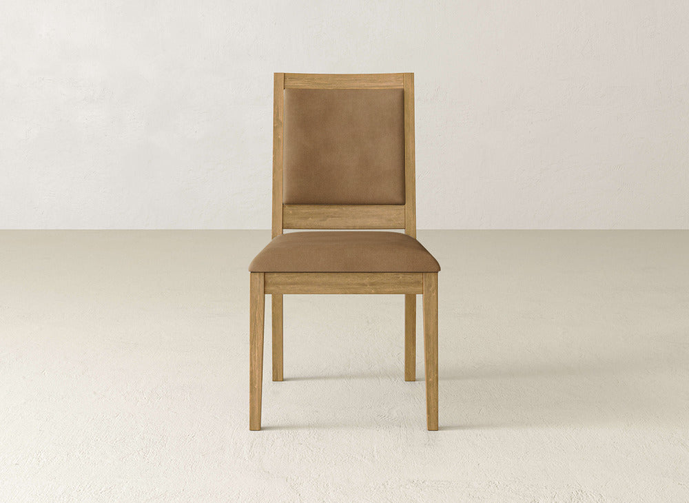 The James+James Gina Side Dining Chair has a maple wood frame and tan upholstered seat and backrest, shown facing forward in a minimalist, light-colored room.