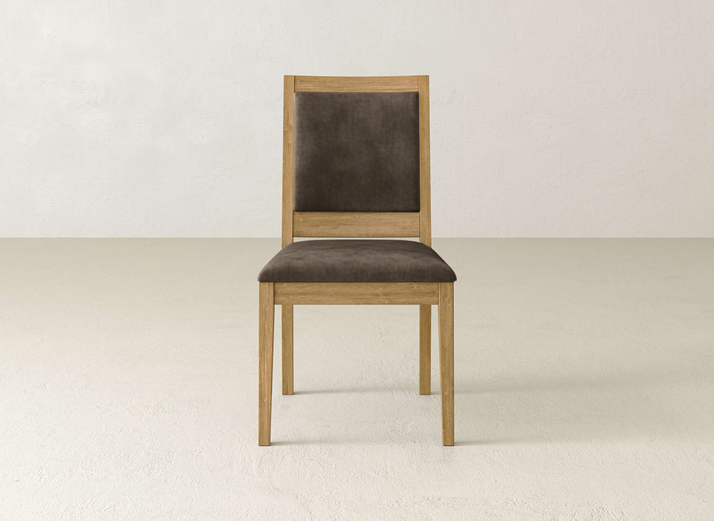 The James+James Gina Side Dining Chair, made of maple wood with a brown cushioned seat and backrest, showcases a simple, modern design against a neutral wall and floor.