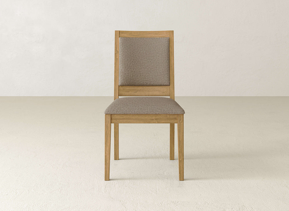 The Gina Side Dining Chair by James+James features a light brown maple wood frame with padded fabric seat and backrest, shown on a light-colored floor against an off-white wall.