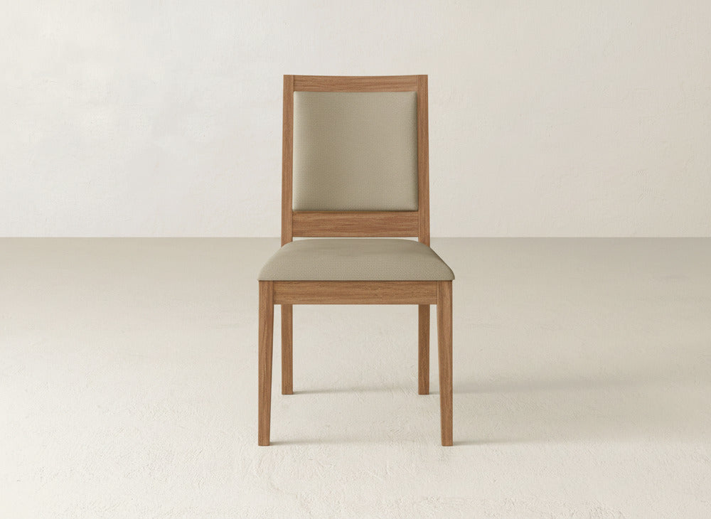 A James+James Gina Side Dining Chair with a beige cushioned seat and backrest in maple wood is centered in a minimal, light-colored room with plain walls and floors.