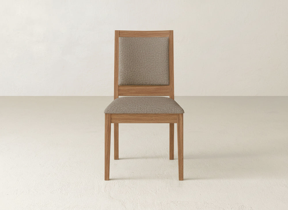 The Gina Side Dining Chair by James+James features a simple design with a padded seat and backrest in light brown fabric, crafted from maple wood and set against a plain light-colored background.