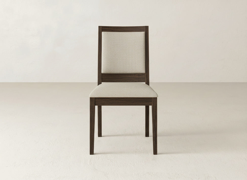 The Gina Side Dining Chair by James+James has a dark brown maple wood frame with a light beige upholstered seat and backrest, shown on a light floor against an off-white wall.