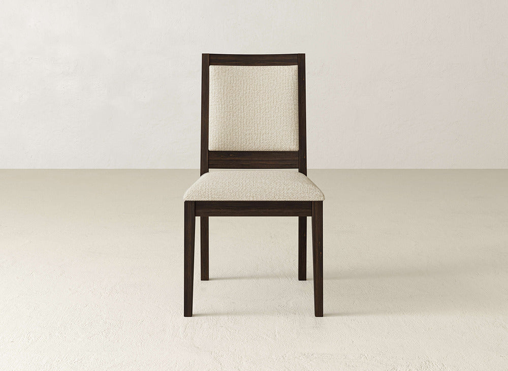 The Gina Side Dining Chair by James+James features a dark brown maple wood frame and light beige cushioned seat and backrest, shown on a light floor against an off-white wall.