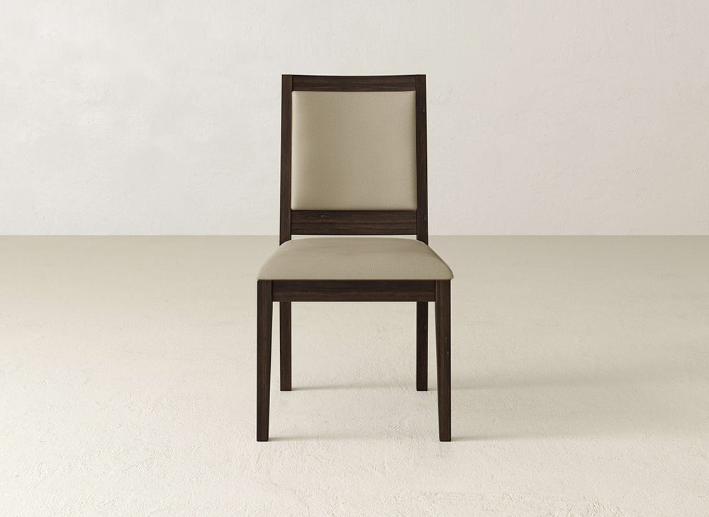 A James+James Gina Side Dining Chair, featuring a beige cushioned seat and backrest with maple wood construction, sits on a light floor against an off-white wall.