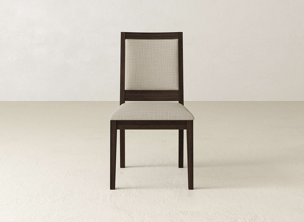 A James+James Gina Side Dining Chair with a dark brown maple wood frame and light beige upholstered seat and backrest sits on a light-colored floor against an off-white wall.