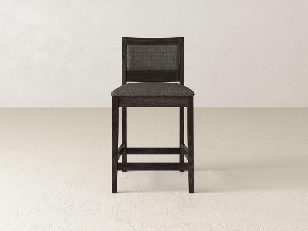 The Gina Side Stool by James & James features a modern design crafted from maple wood, highlighted by a dark finish, rectangular backrest, and gray fabric-upholstered padded seat.