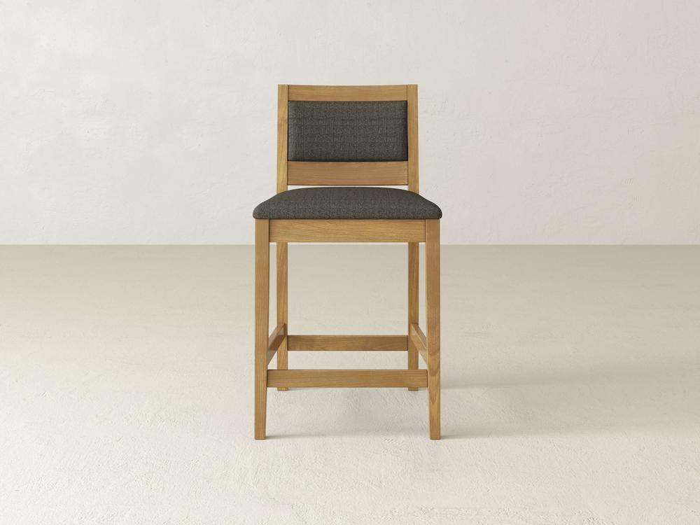 The Gina Side Stool by James & James is a modern design masterpiece, showcasing a dark grey cushioned seat and backrest on sleek maple wood. Its minimalist silhouette with clean lines contrasts beautifully against the light backdrop.