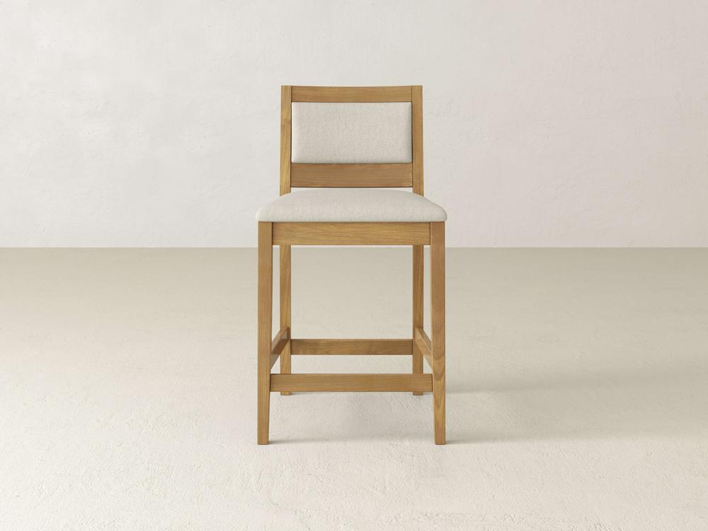 The Gina Side Stool by James & James boasts a modern design, featuring a maple wood construction with a beige upholstered seat and backrest, set against a light-colored background.