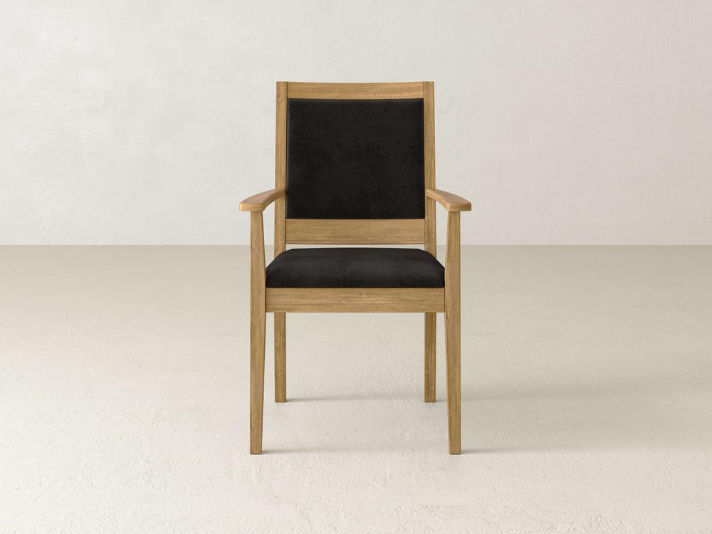 A wooden chair with black cushioned seat and backrest is centered against a plain light-colored background.