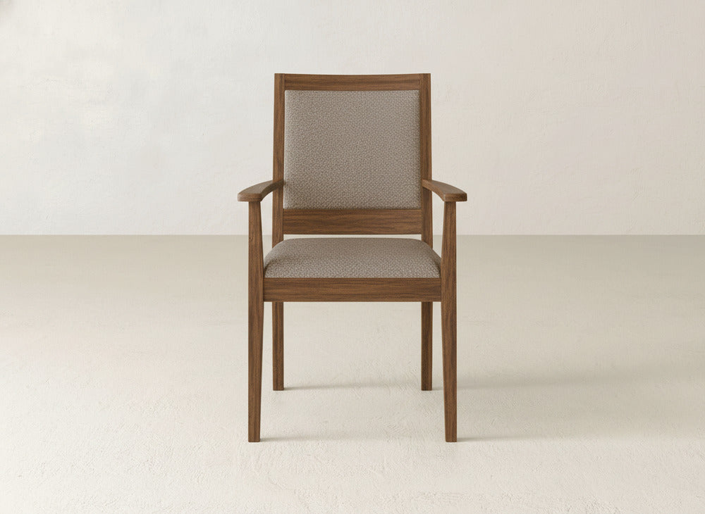 The Gina Arm Dining Chair by James+James is a modern piece made of maple, with a light brown upholstered seat and backrest, shown in a minimalist space with off-white walls and floors.
