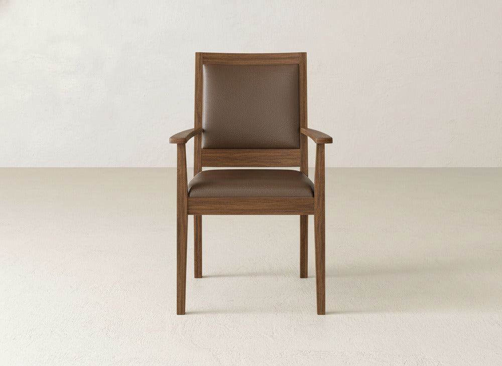 The Gina Arm Dining Chair by James+James is a modern maple wood dining chair with armrests and brown cushioned seat and backrest, shown against a plain light-colored wall and floor.