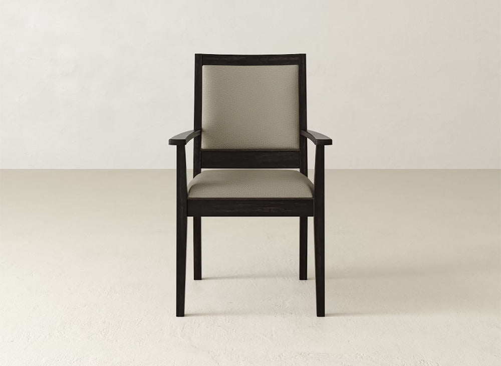 The Gina Arm Dining Chair by James+James features a dark maple wood frame with a light beige padded seat and backrest, set against a plain, light-colored wall and floor.