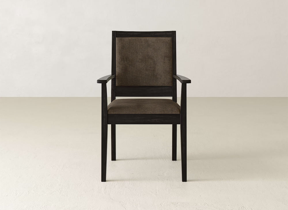 The Gina Arm Dining Chair by James+James features square maple armrests and legs with a dark brown cushioned seat and backrest, set against a plain light-colored wall and floor.