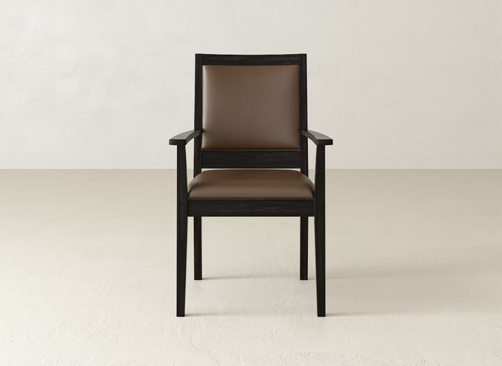 A front view of the Gina Arm Dining Chair by James+James—a brown cushioned, contemporary seat with dark maple frame and armrests—set against a plain light wall and floor.
