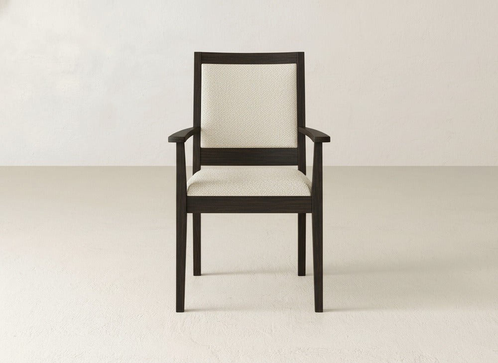 The Gina Arm Dining Chair by James+James features a dark maple wood frame and light upholstered seat and backrest, shown centered in a minimalist, light-toned room.