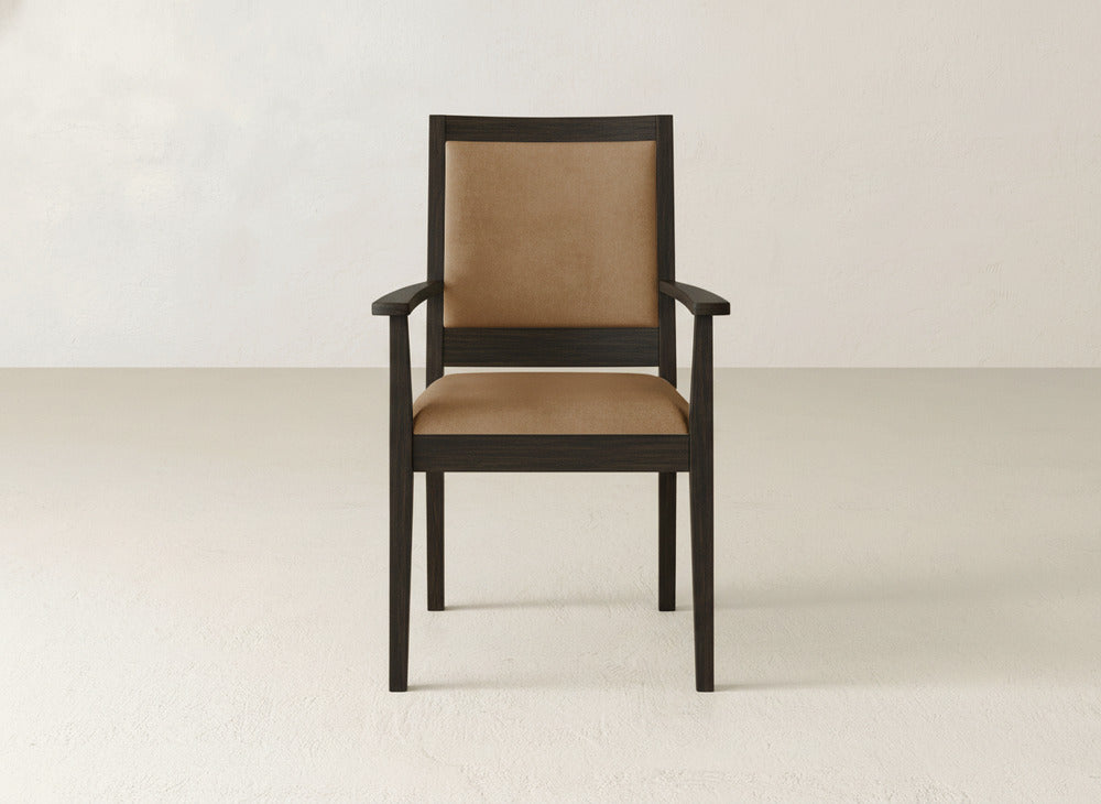 The James+James Gina Arm Dining Chair, featuring a dark maple frame and tan upholstered seat and backrest, is positioned against a plain, light-toned wall and floor.