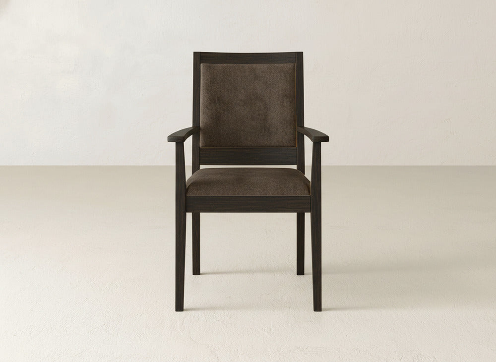 The James+James Gina Arm Dining Chair is a contemporary piece with a dark maple frame, armrests, square backrest, and padded brown fabric seat, displayed on a light floor against an off-white wall.