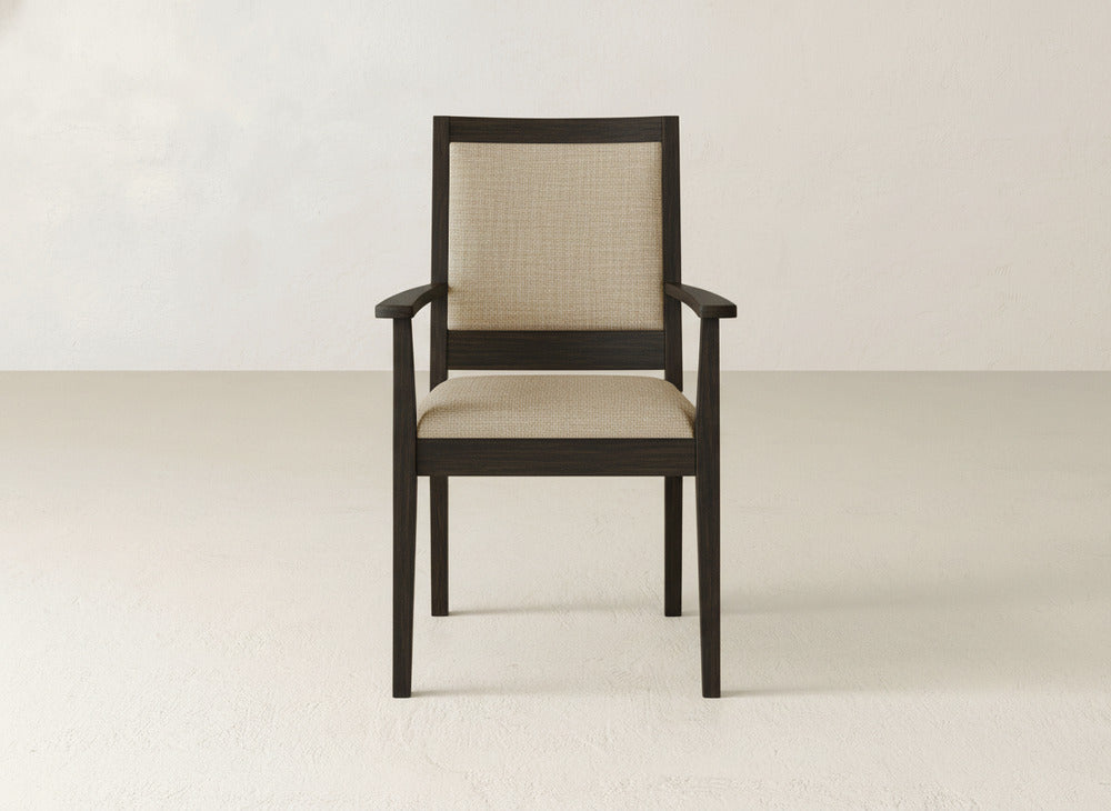 The James+James Gina Arm Dining Chair is a modern piece with a dark maple wood frame and light beige upholstered seat and backrest, shown on a plain light floor with a neutral wall background.