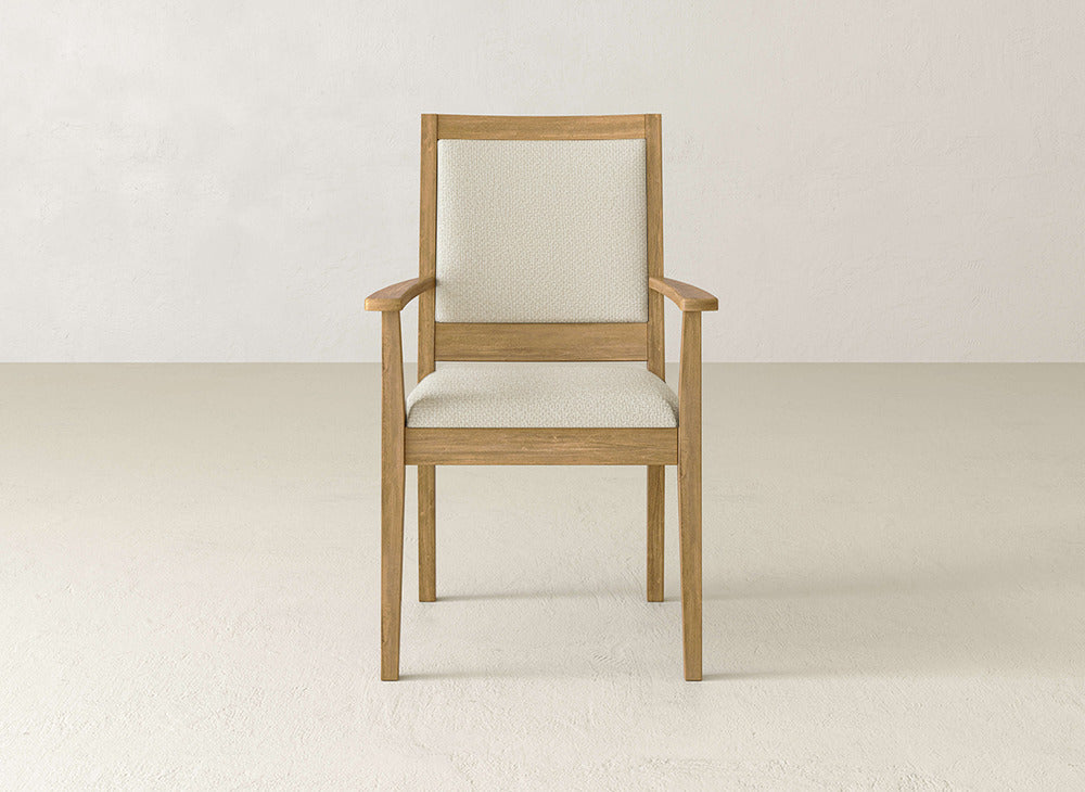 The James+James Gina Arm Dining Chair features straight maple wood legs and a beige upholstered seat and backrest, shown on a light floor with a plain, light wall backdrop.