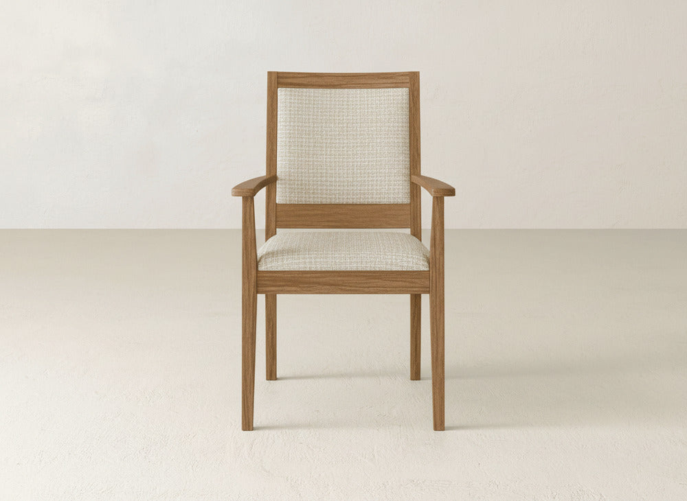 The Gina Arm Dining Chair by James+James is a modern maple wood chair with armrests and a cushioned light beige upholstered seat and backrest, shown against a plain, light-colored wall and floor.