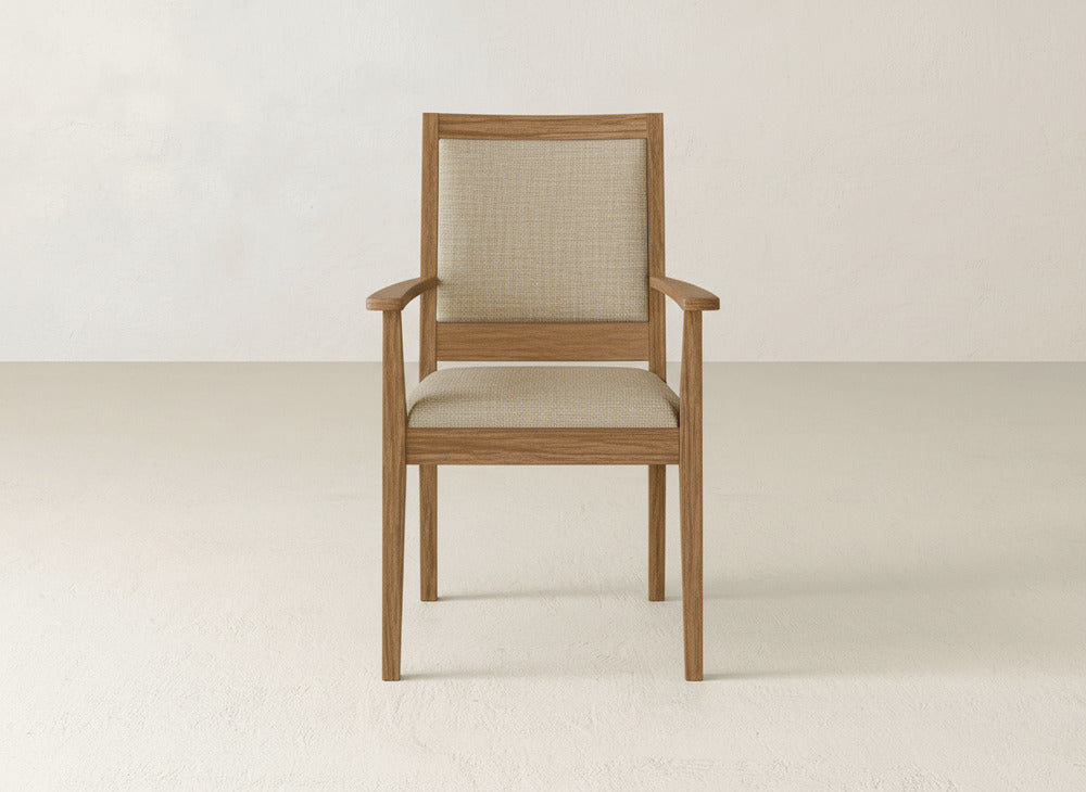 The Gina Arm Dining Chair by James+James features a light brown maple wood frame with a beige upholstered seat and backrest, shown against a plain, light-colored wall and floor.