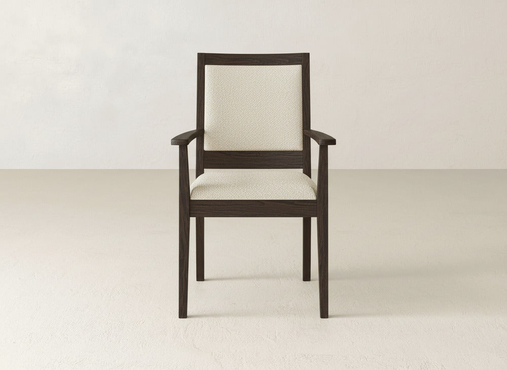 The Gina Arm Dining Chair by James+James features a contemporary design with a dark brown maple wood frame and light cream upholstered seat and backrest, displayed against an off-white wall and floor backdrop.