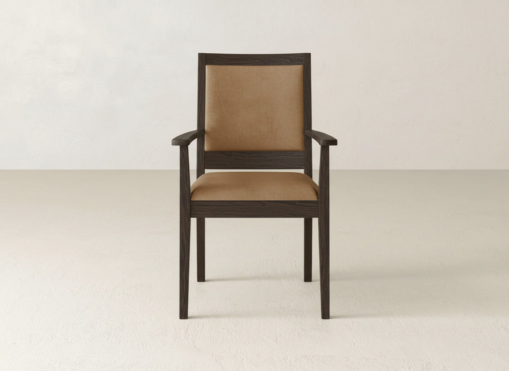 The James+James Gina Arm Dining Chair, a modern piece crafted from maple wood, features a brown upholstered seat and backrest and is shown on a light floor against an off-white wall.