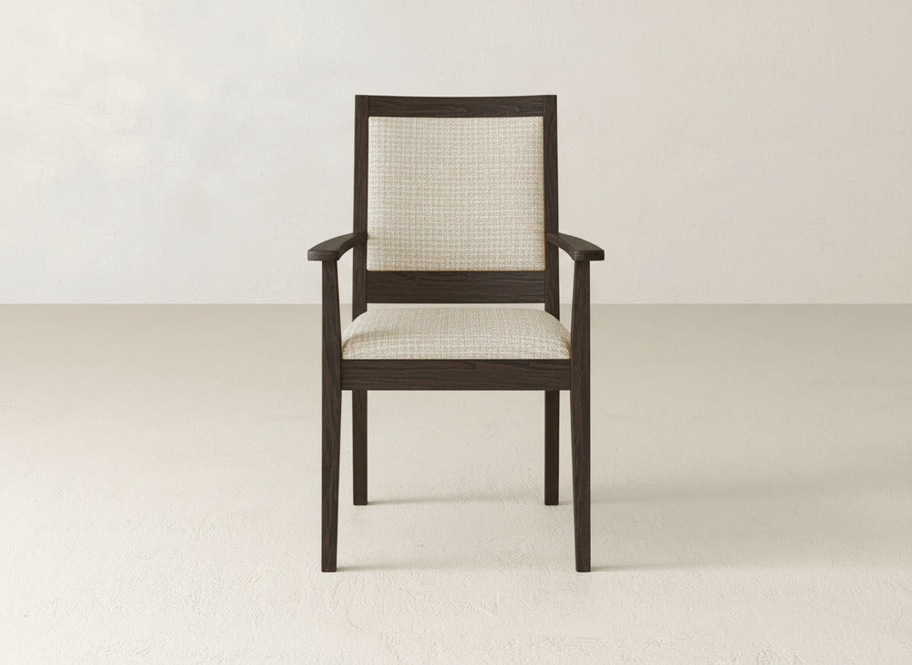 The Gina Arm Dining Chair by James+James features a dark maple frame with straight arms and legs, plus a light, textured upholstered seat and backrest, shown against a simple, light-toned wall and floor.
