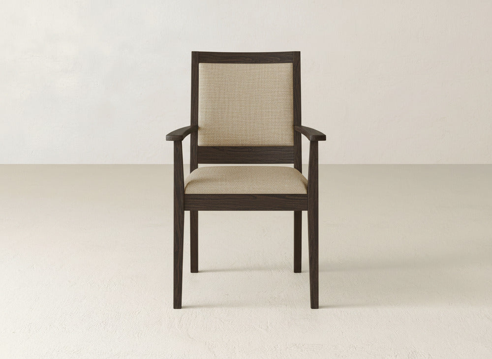 The James+James Gina Arm Dining Chair showcases a dark brown maple frame, beige upholstered seat and back, and straight armrests, set on a light floor against an off-white wall.