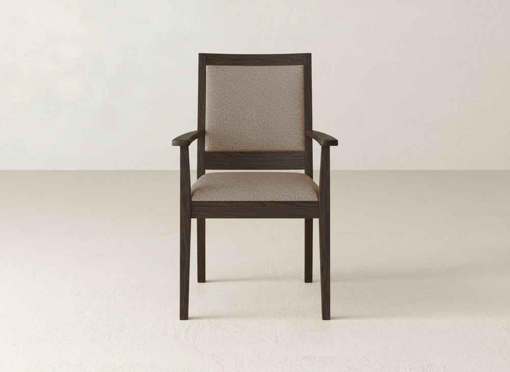 The Gina Arm Dining Chair by James+James is a modern maple wood chair with armrests and light beige upholstered seat and back, shown centered against a plain, light-toned wall and floor.