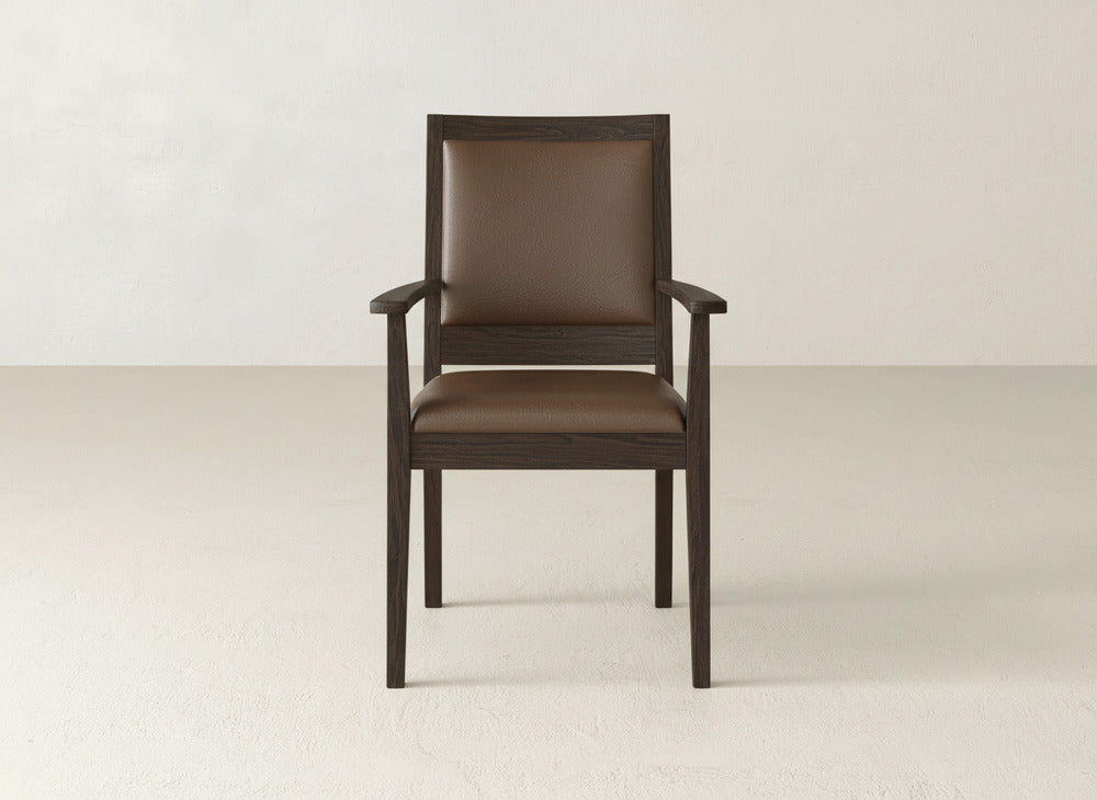 The James+James Gina Arm Dining Chair boasts a dark maple wood frame, armrests, and a brown cushioned seat/backrest—ideal for contemporary dining spaces. Pictured on a light floor against an off-white wall.