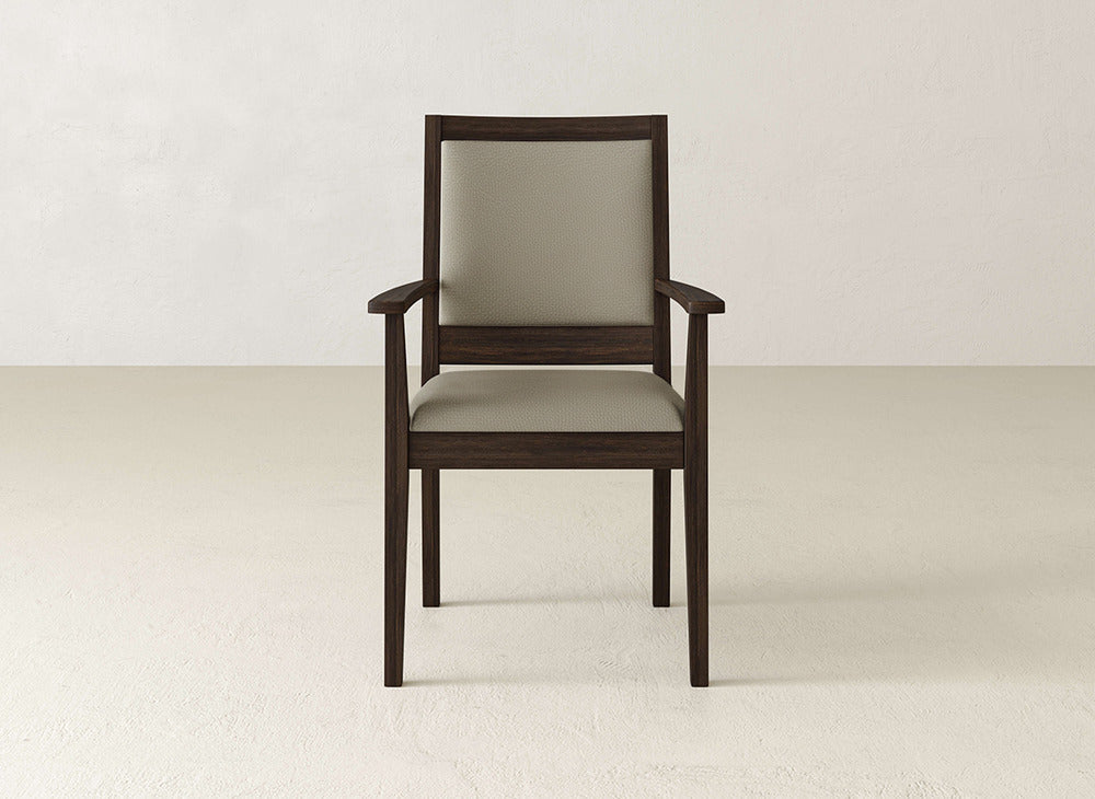 The James+James Gina Arm Dining Chair is a modern maple chair with armrests and a padded beige seat and back, shown on a light floor against an off-white wall.
