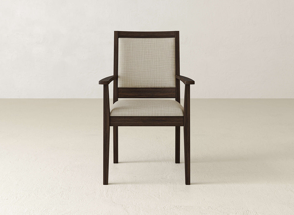 The Gina Arm Dining Chair by James+James features a dark brown maple frame with a light beige upholstered seat and backrest, shown on a light floor against a neutral wall.