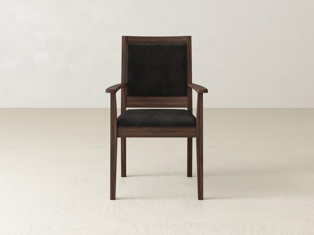 A wooden armchair with a dark cushioned seat and backrest, set against a plain, light-colored wall. The chair features sleek, simple lines and a minimalist design, with prominent armrests and a sturdy frame.