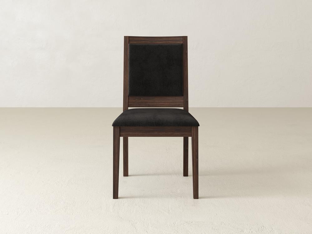 Wooden chair with a black cushioned seat and backrest, centered against a plain, light gray background.