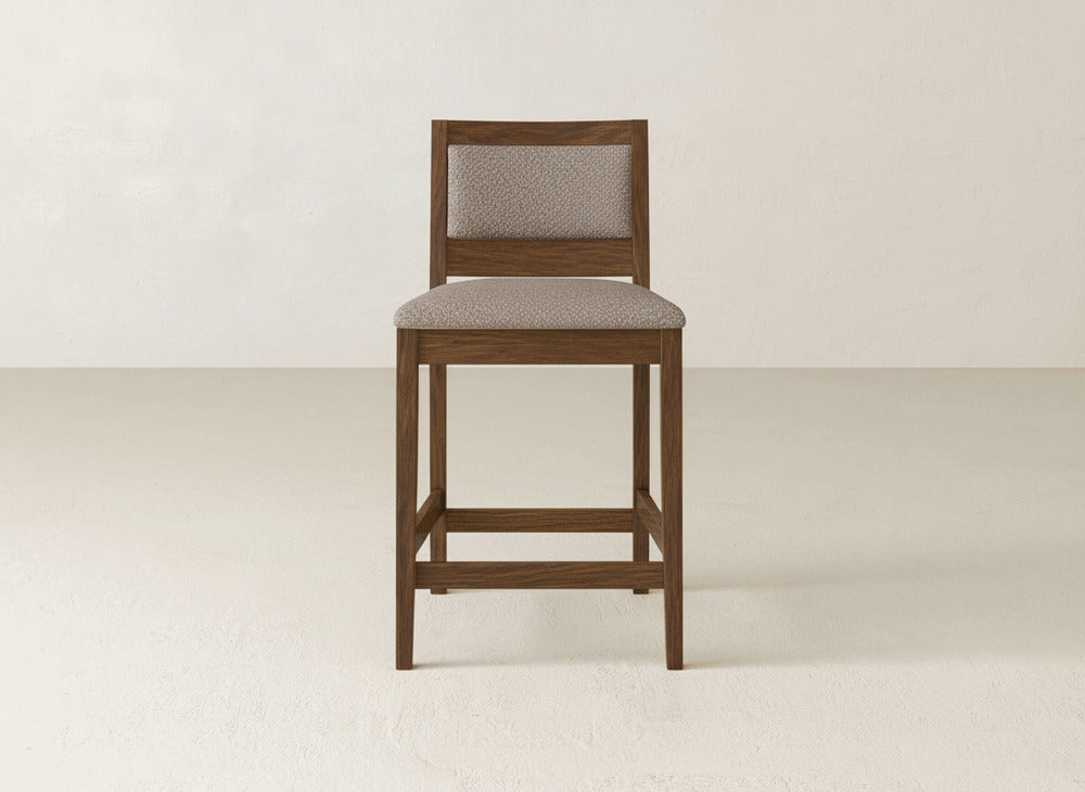 The Gina Side Stool by James & James showcases a modern design with cushioned seat and backrest in light gray fabric, crafted from elegant maple wood, displayed on a plain off-white background.