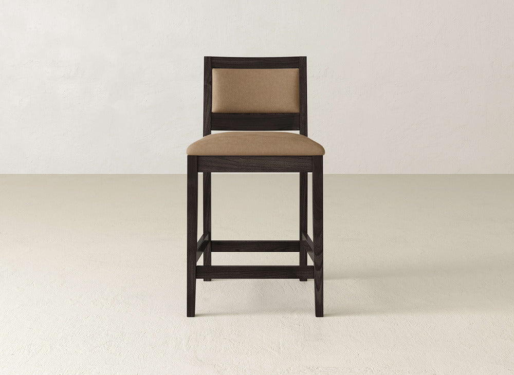 The Gina Side Stool by James & James features maple wood with a tan cushioned seat and backrest, displayed against a light wall and floor, bringing modern style to any space.