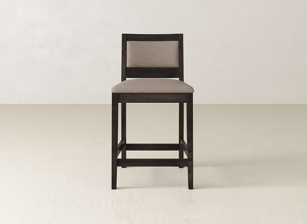 The Gina Side Stool by James & James features a modern design with a dark maple wood frame and light beige upholstered seat and backrest, set on a light floor against an off-white wall.
